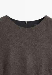 Detailní záběr na hnědý herringbone výstřih šatů s černým podšitím a stříbrným táhlem zipu umístěným uprostřed zadního límce.