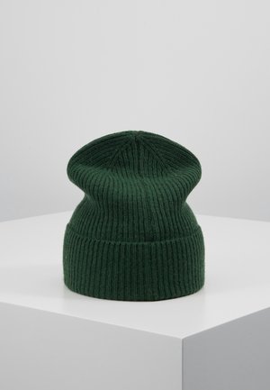 Bonnet en tricot côtelé vert foncé avec revers replié, posé sur une surface blanche sur un fond uni clair.