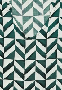 Grön och vit geometrisk mönstrad tyg med vinklade zigzag-former i varierande nyanser, med en mjuk, slät textur och rundad halsringning.