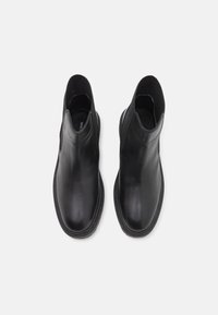 Botas de tobillo de cuero negro con una textura suave, paneles laterales elásticos y punta redondeada. Presenta una suela baja y duradera.