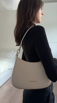 Valentino-tas van zacht beige leer, met een gebogen vorm, verstelbare riem en metalen beslag. Logo geperst op de voorkant.