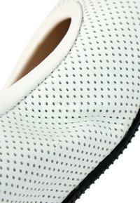 Gros plan sur une tige de chaussure en cuir blanc perforé avec coutures visibles et bord de semelle noire.