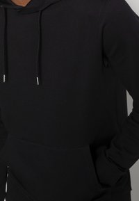 Schwarzer Kapuzenpullover mit Kängurutasche, Zugkordel mit metallischen Enden und gerippten Bündchen. Hergestellt aus weichem, elastischem Stoff.