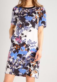 Vestido corto de manga corta con estampado floral que presenta una base blanca con patrones en azul, rosa y negro. Confeccionado con una tela ligera, de diseño minimalista.