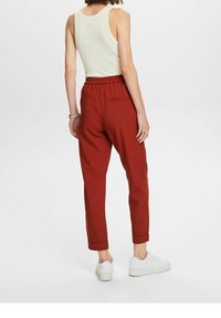 Czerwone spodnie o luźnym kroju z elastycznym pasem i podwiniętymi nogawkami, zestawione z jasnym topem na ramiączkach i białymi trampkami.