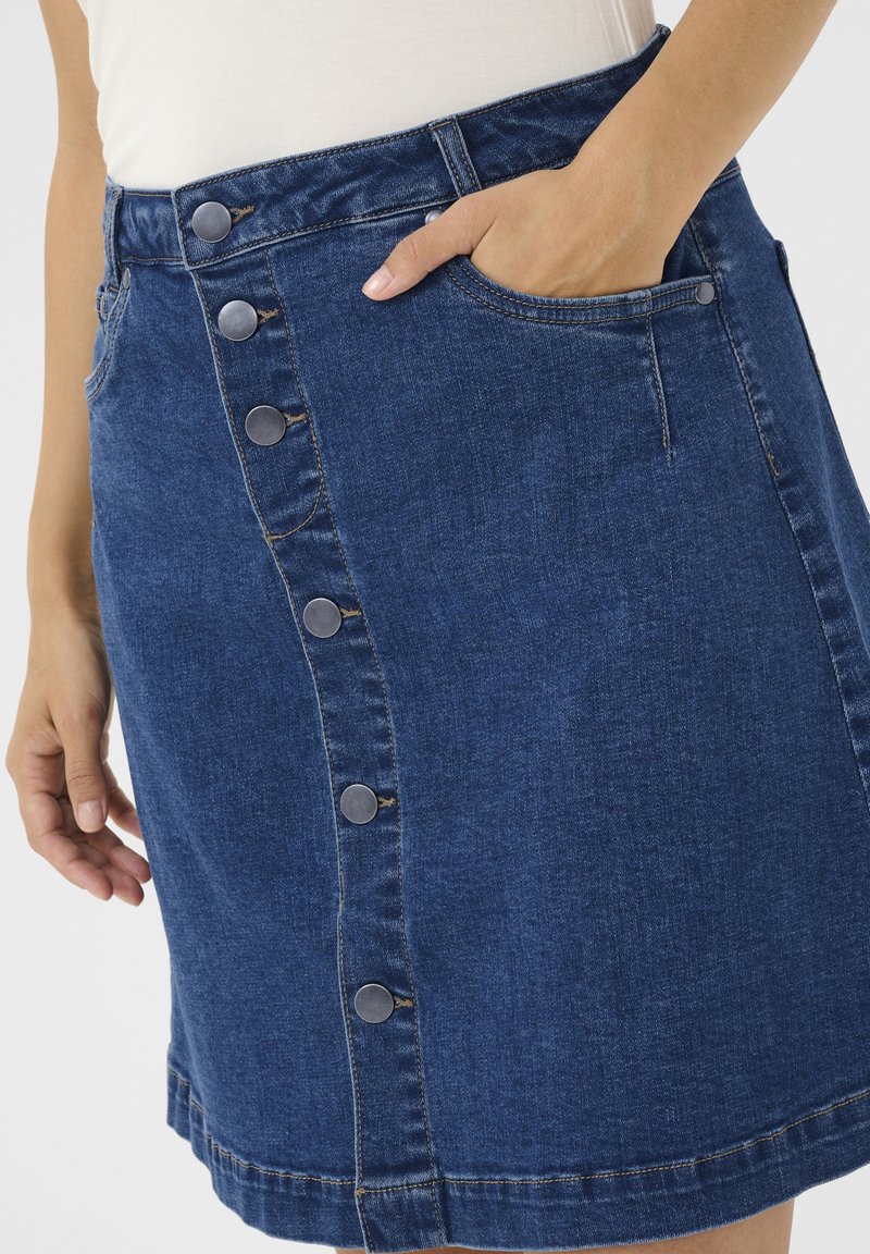 Jeanskjol med rak skärning, mörkblå färg, framknappstängning med silverdetaljer, sidofickor och synliga sömdetaljer.