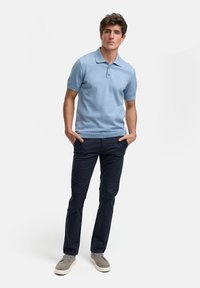 Polo de punto azul claro con mangas cortas, confección de dos botones, combinado con chinos azul marino y zapatos casuales grises. Diseño sencillo y limpio.