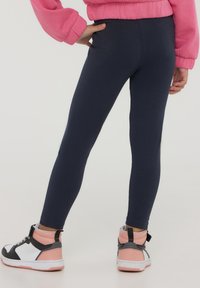 Granatowe legginsy o gładkiej fakturze. Połączone z różowo-czarnymi butami sportowymi za kostkę z białym akcentem i czarnym paskiem.
