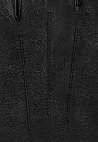 Czarne skórzane rękawiczki z trzema przeszyciami na tyle, prezentujące fakturowaną powierzchnię i dopasowany krój, zaprojektowane z myślą o funkcjonalności.