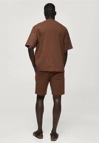 Ensemble t-shirt en coton marron et shorts, design simple, manches courtes, coupe décontractée, tissu texturé, porté avec des sandales marron.