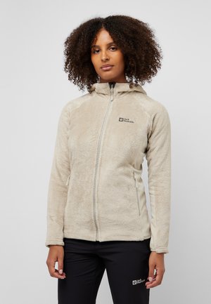 Veste en polaire beige avec capuche, fermeture éclair sur le devant et texture douce. Présente un logo sur la poitrine et un col clair contrastant.