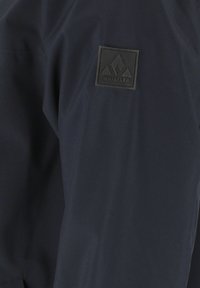 Musta takin hiha, jossa on koholla oleva musta suorakulmainen merkki, jossa on vuoristologo ja sana "WHISTLER".