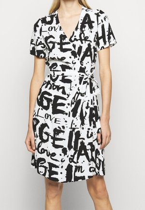 Robe portefeuille blanche avec texte noir style graffiti et motifs abstraits, manches courtes, encolure en V et ceinture à nouer sur le côté.