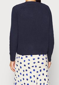 Navy blue, knitted sweater with raglan sleeves. Soft texture, ribbed hem, worn over a cream skirt with blue polka dots.