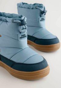 Blaue gesteppte Schneestiefel mit einem gerafften Schaft, ausgestattet mit strukturierten dunkelblauen Akzenten und einer tanfarbenen Gummisohle. Das "Paw Patrol"-Logo ist sichtbar.