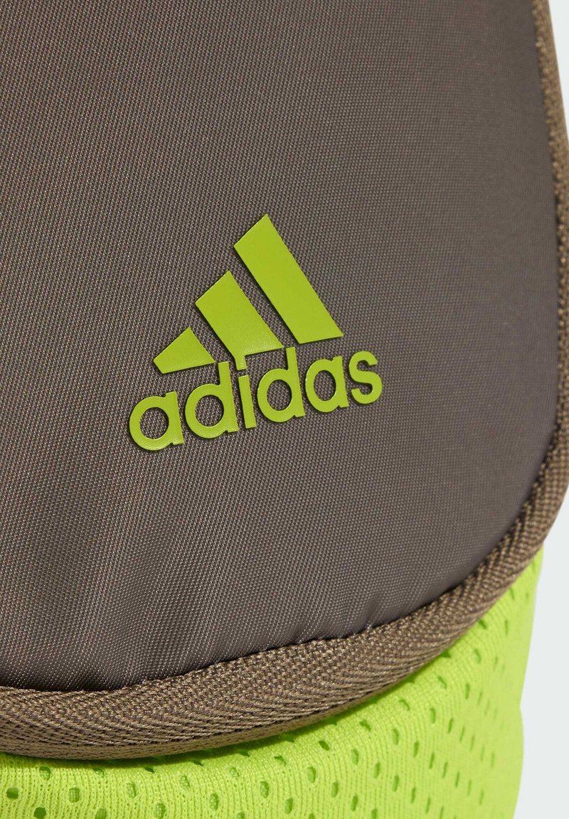 Nahaufnahme von braunem und neongrünem Stoff mit einem hellgrünen Adidas-Logo auf strukturierter Oberfläche.