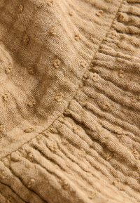 Strukturiertes beiges Gewebe mit einem weichen, gerippten Design. Es enthält kleine, erhabene Punkte und subtile Variationen in der Webart, die eine taktile Oberfläche schaffen.