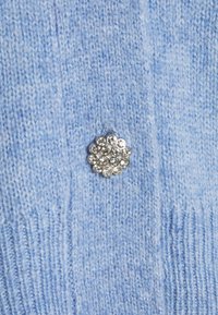 Ljusblå stickad tyg med vertikal ribbning, prydd med en silverblomma i mitten dekorerad med klara rhinestones.