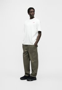 Λευκό βαμβακερό t-shirt με μικρό ροζ λογότυπο, συνδυασμένο με φαρδιά παντελόνια σε ανοιχτό ελαιόχρωμο και μαύρα αθλητικά παπούτσια, με ορατές τσέπες.