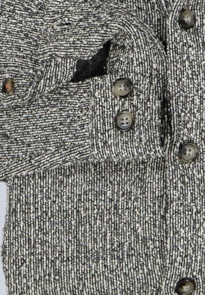 Grau-weißer Strickpullover mit einem strukturierten Muster, fünf dunklen Knöpfen und einer Seitentasche. Das Material wirkt weich und warm.