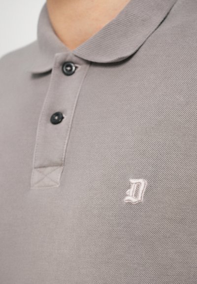 Γκρι πόλο μπλούζα με ριμπ ύφασμα, διαθέτει διπλωμένο γιακά, δύο μαύρα κουμπιά και ένα μικρό κεντημένο γράμμα "D" σε ανοιχτό ροζ στο στήθος.