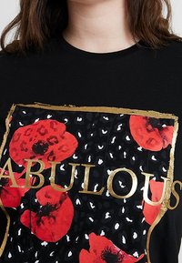 Camiseta negra con diseño de amapola roja y estampado de leopardo, con la palabra "FABULOSA" en letras doradas. Cuello redondo y mangas cortas.