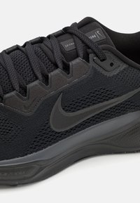 Schwarzer Sport Schuh mit einem strukturierten Mesh-Obermaterial, flexibler Sohle und verstärkter Ferse. Mit schwarzen Schnürsenkeln und einem dezenten Logo-Akzent.
