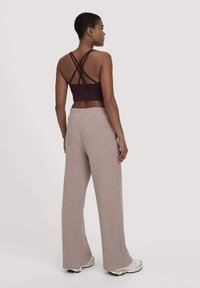 Bordeauxrotes Cropped-Top mit überkreuzten Trägern, kombiniert mit hellbraunen weit geschnittenen Hosen. Weicher Stoff, lockere Passform, seitliche Taschen und sportliche Schuhe.
