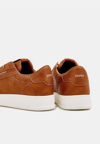 Beżowe skórzane trampki z białymi podeszwami, wyposażone w subtelne przeszycia, wyściełany kołnierz oraz oznaczenia na pięcie i boku.