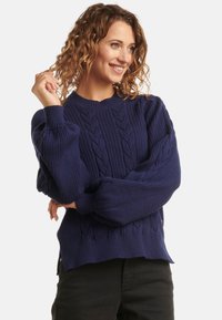 Navy blue cable-knit sweater featuring ribbed details, crew neckline, and balloon sleeves; textured fabric with a relaxed fit.