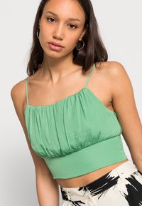 Top cropped verde em tecido suave, com um corpete pregueado e alças finas. Combinado com calças de cintura alta estampadas.