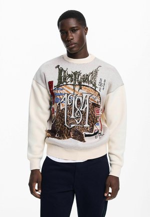 Kötött pulóver krémszínű testtel és színes grafikával, amely állatokat és szöveget ábrázol. A bordázott mandzsetták és az alsó szegély szabályosillik.