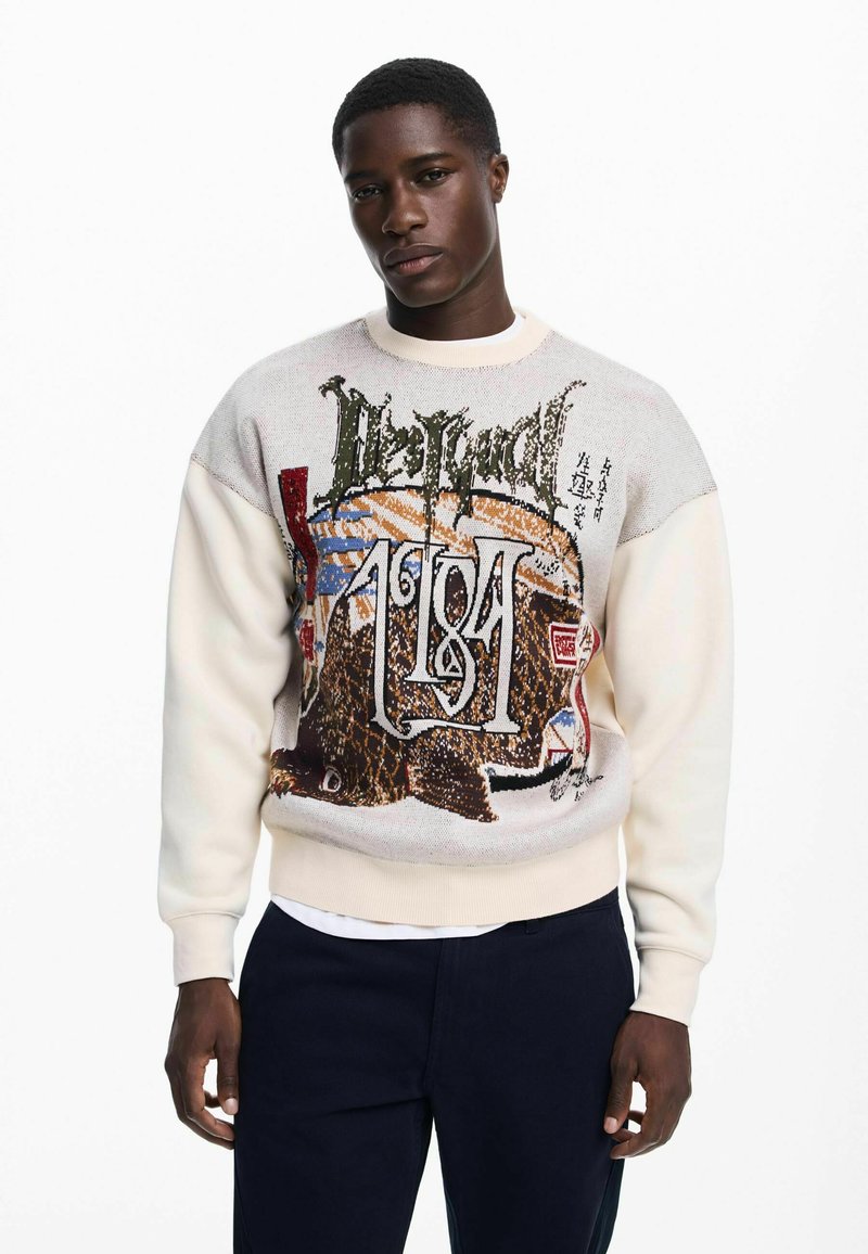 Kötött pulóver krémszínű testtel és színes grafikával, amely állatokat és szöveget ábrázol. A bordázott mandzsetták és az alsó szegély szabályosillik.