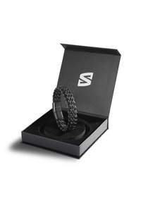 Black chain bracelet displayed in a black box with a soft interior, featuring a metal clasp and a logo on the box lid.