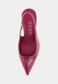 Zapato de charol rosa con slingback, punta afilada, acento de logotipo triangular dorado y textura suave. El interior presenta la marca "GUESS".