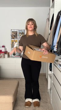 Brown short-sleeve shirt, black flared pants, and brown slip-on shoes with white fur lining. Holding a Zalando cardboard box.