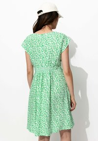 Robe verte avec un imprimé floral, manches courtes à volants et taille smockée. Tissu doux et design arrivant aux genoux.