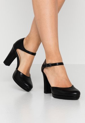 Chaussures à talons hauts noires avec un bout arrondi, une bride de cheville, une texture en cuir lisse et un design à talon épais.