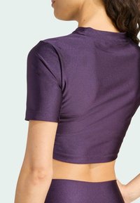 Top corto de manga corta en color púrpura, fabricado en un tejido brillante y suave con un diseño ajustado que expone una pequeña sección del abdomen.