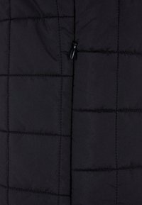 Veste rembourrée noire au design matelassé, dotée de coutures horizontales et d'une poche zippée. Le matériau semble lisse et léger.