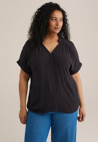Čierna, textúrovaná, blúzka s krátkymi rukávmi a výstrihom do V, v kombinácii s vysokými modrými nohavicami.