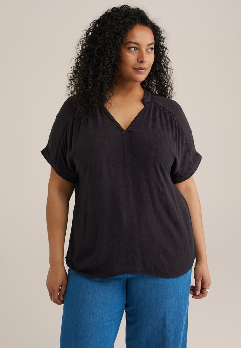 Blusa nera, testurizzata, a maniche corte con scollatura a V e maniche arrotolate, abbinata a pantaloni blu a vita alta.