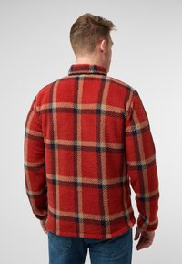 Rode fleece jas met een geruit patroon van beige en marineblauwe lijnen, een kraag en een relaxte pasvorm, gedragen met blauwe jeans.