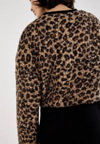Pull en tissu fuzzy avec imprimé léopard, présentant un motif marron foncé, noir et beige, avec des manches longues et un ourlet en tricot noir.