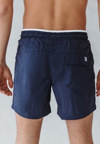 Marineblauwe zwembroek gemaakt van lichtgewicht stof, met een elastische tailleband, een achterzak met knoop en een klein logodetail.