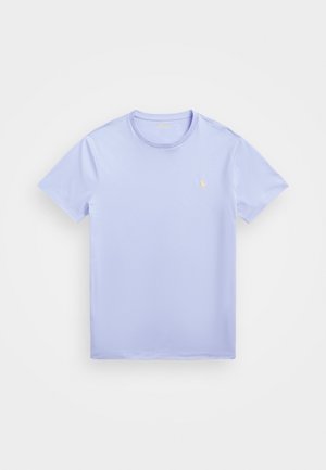 Camiseta de algodón de color púrpura claro con cuello redondo, mangas cortas y un pequeño logotipo bordado amarillo en el lado izquierdo del pecho. Textura suave.