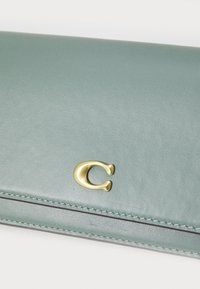 Green leather wallet with a smooth texture, featuring a gold "C" logo and contrasting stitching along the edges.