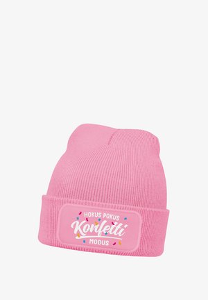 Pink knitted beanie with folded cuff featuring a rectangular patch with white text "Hokus Pokus Konfetti Modus" and colorful confetti accents.