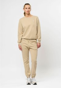 Beige tröja och byxor set, tillverkat av mjukt material. Tröjan har en rund hals och ribbade ärmslut; byxorna har ett justerbart snöre och elastiska anklar.