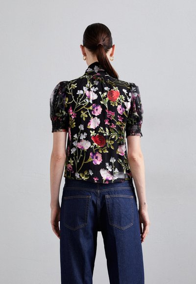 Black floral blouse with puff sleeves, featuring colorful flower patterns and lace trim. Paired with dark denim jeans.